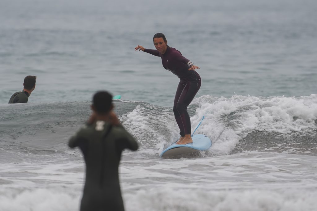 Surfeur débutant surfant sur une petite vague avec un instructeur de surf sur la plage