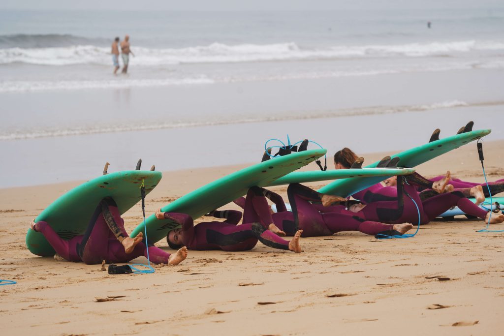 Surfschüler unter ihren Surfbrettern am Strand