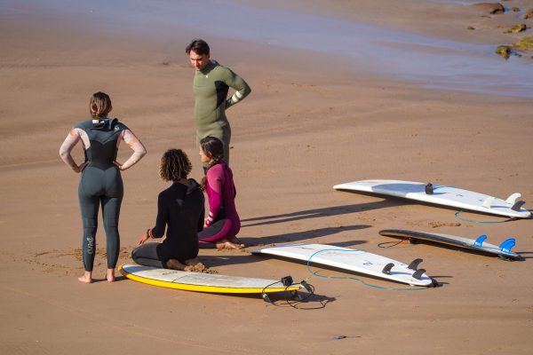 Surfcoach talks to surf students sitting on the beach with surfboards
