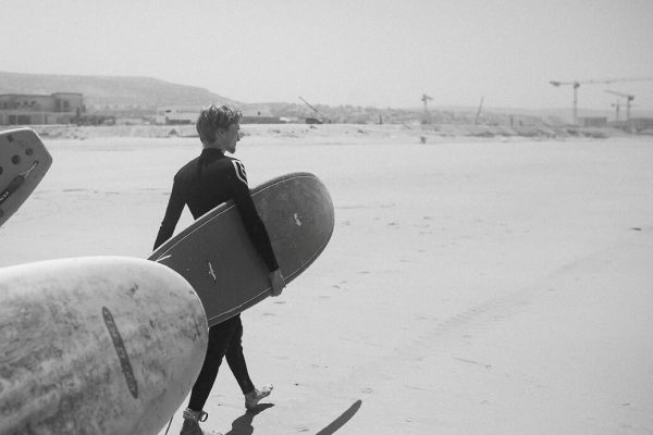 Photo en blanc et noir d'un surfeur marchant sur la plage avec sa planche de surf.